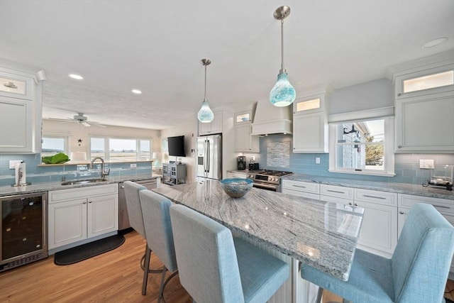 kitchen featuring premium range hood, wine cooler, appliances with stainless steel finishes, white cabinets, and a sink