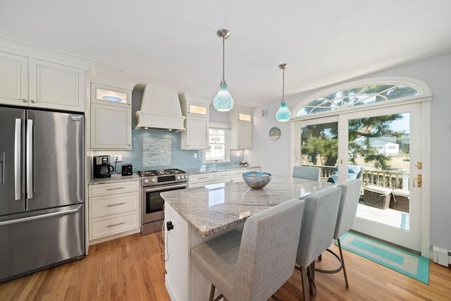 kitchen featuring a kitchen island, light stone countertops, premium range hood, appliances with stainless steel finishes, and white cabinets