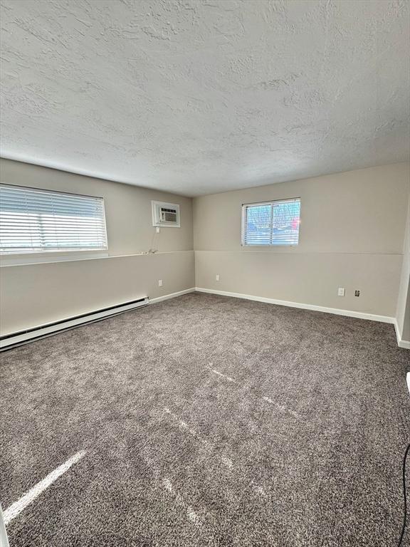 unfurnished room featuring carpet, a healthy amount of sunlight, an AC wall unit, and baseboard heating