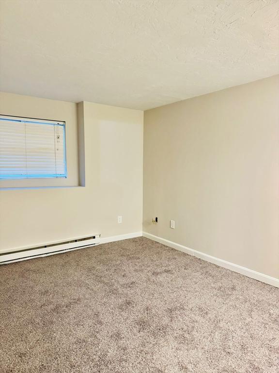 carpeted spare room with a baseboard radiator and a textured ceiling