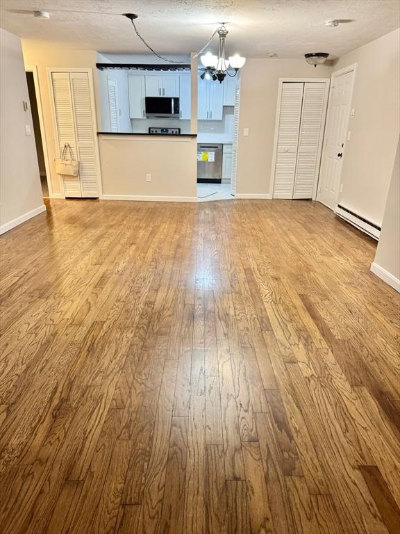 unfurnished living room featuring a baseboard radiator, a chandelier, a textured ceiling, and light wood-type flooring