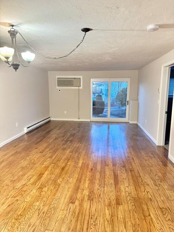 unfurnished living room featuring hardwood / wood-style floors, a wall mounted air conditioner, a chandelier, a baseboard heating unit, and a textured ceiling