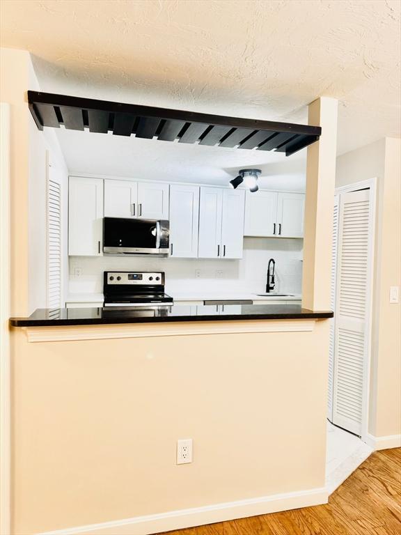 kitchen with sink, light hardwood / wood-style flooring, white cabinetry, stainless steel appliances, and a textured ceiling