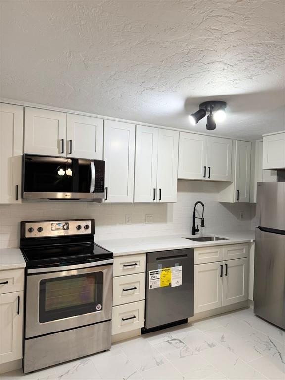 kitchen with white cabinetry, sink, backsplash, stainless steel appliances, and a textured ceiling