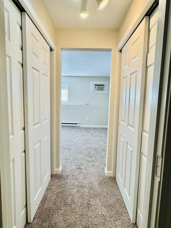 hallway with a wall unit AC, light carpet, and baseboard heating