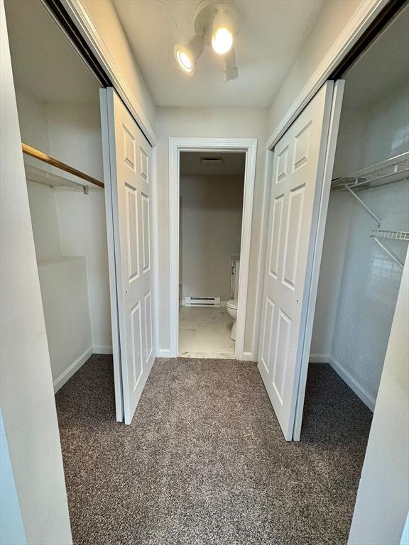 hallway featuring baseboard heating and dark colored carpet