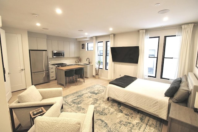 bedroom featuring stainless steel fridge, sink, and light wood-type flooring