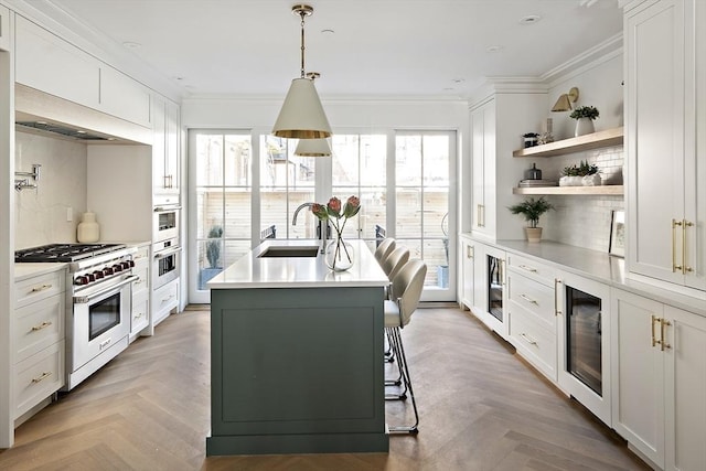 kitchen featuring high end stainless steel range, white cabinets, sink, a kitchen island with sink, and parquet floors