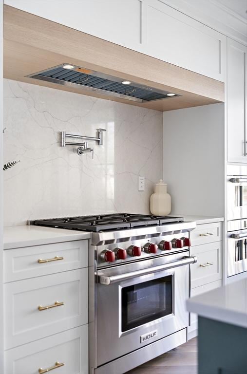 kitchen with hardwood / wood-style flooring, stainless steel appliances, white cabinets, and tasteful backsplash