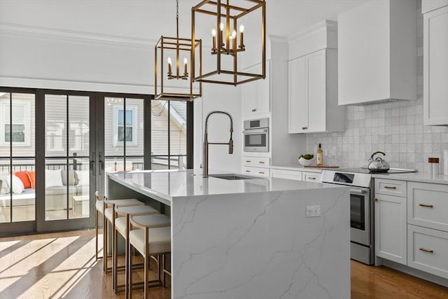 kitchen with an island with sink, appliances with stainless steel finishes, wall chimney exhaust hood, white cabinets, and sink