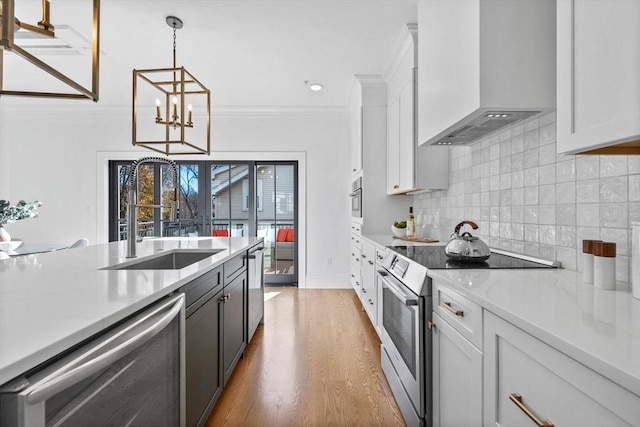 kitchen with appliances with stainless steel finishes, wall chimney exhaust hood, decorative light fixtures, white cabinetry, and sink