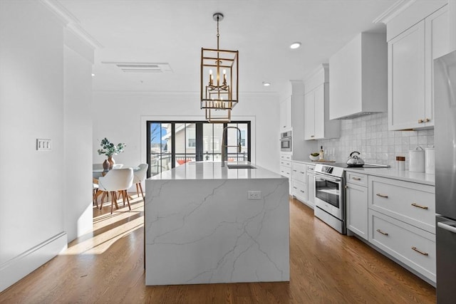 kitchen featuring white cabinets, appliances with stainless steel finishes, an island with sink, and pendant lighting