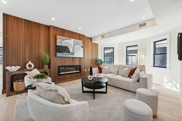 living area with wood walls, light wood-style flooring, visible vents, and a glass covered fireplace