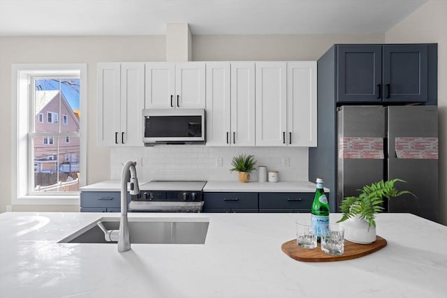 kitchen with tasteful backsplash, light stone counters, appliances with stainless steel finishes, white cabinets, and a sink