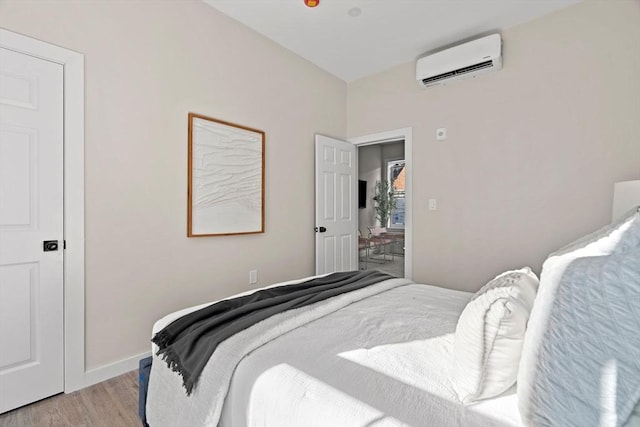 bedroom with light wood finished floors, baseboards, and a wall unit AC