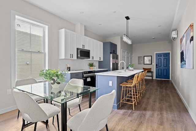 kitchen with light countertops, wood finished floors, hanging light fixtures, stainless steel appliances, and a kitchen island with sink