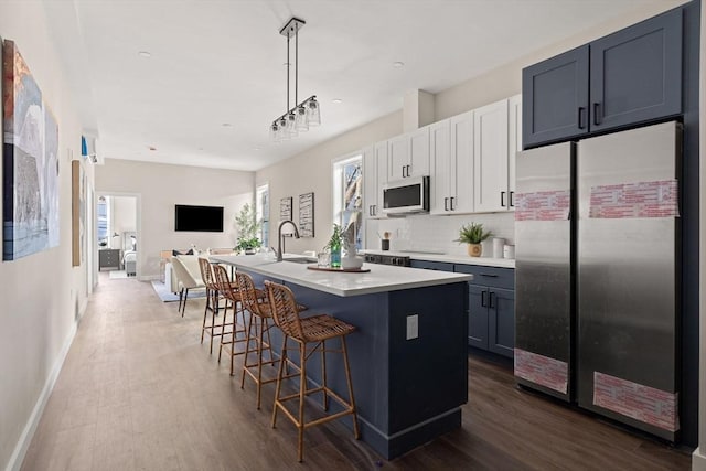 kitchen featuring backsplash, open floor plan, a center island with sink, dark wood-style floors, and stainless steel appliances