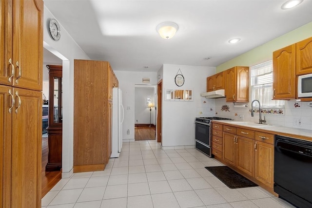 kitchen featuring white appliances, decorative backsplash, light countertops, under cabinet range hood, and a sink