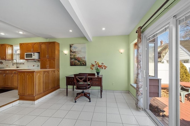 interior space with white microwave, beamed ceiling, light countertops, backsplash, and light tile patterned flooring