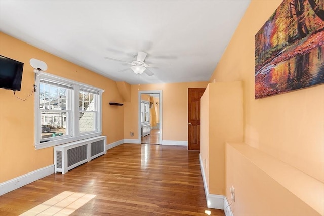 interior space with baseboards, wood finished floors, a ceiling fan, and radiator