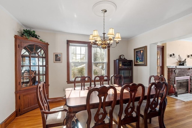 dining space featuring baseboards, light wood-type flooring, a brick fireplace, an inviting chandelier, and crown molding