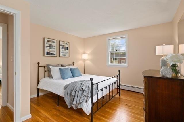 bedroom with light wood-style flooring, baseboards, and a baseboard heating unit