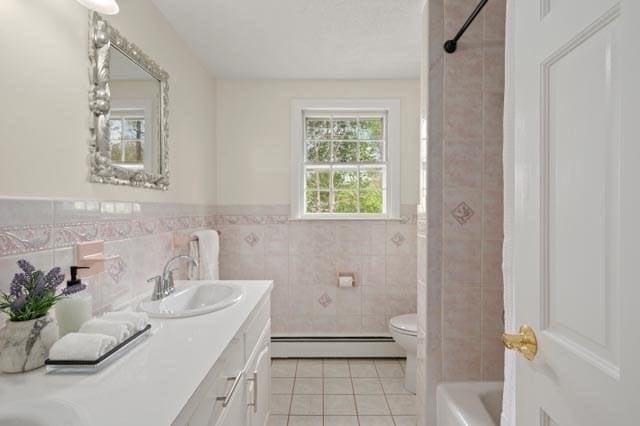 bathroom with tile walls, a baseboard heating unit, wainscoting, a sink, and tile patterned floors