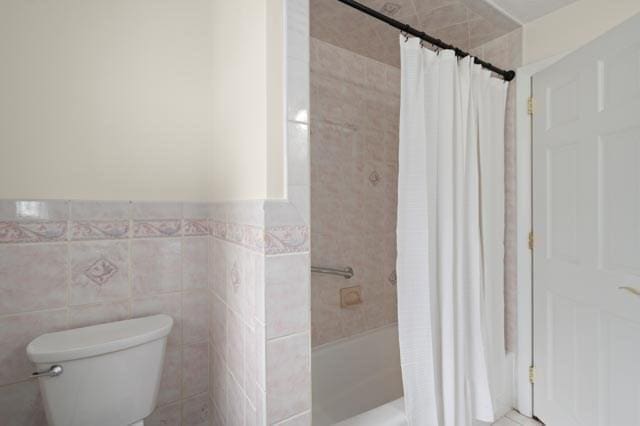 full bath featuring wainscoting, toilet, a shower with shower curtain, and tile walls