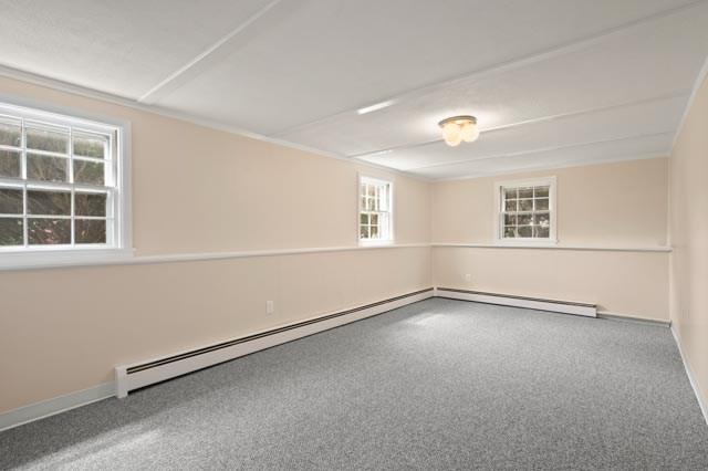 carpeted empty room featuring a baseboard heating unit, baseboards, and a healthy amount of sunlight
