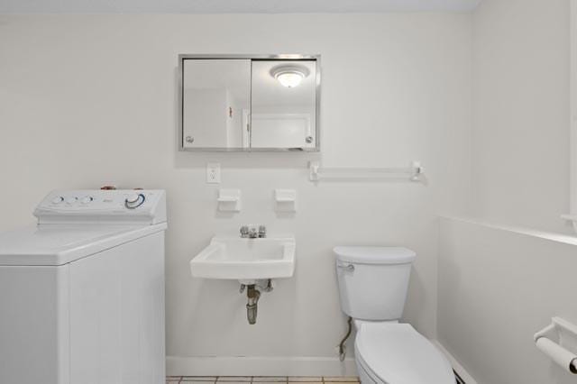 bathroom with toilet, a sink, tile patterned flooring, baseboards, and washer / clothes dryer
