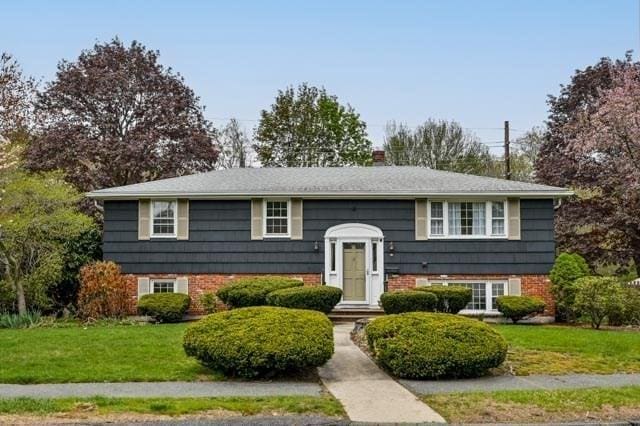 bi-level home with a chimney, brick siding, and a front lawn