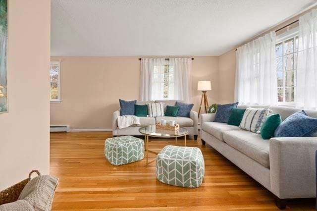 living area with baseboards, baseboard heating, a healthy amount of sunlight, and wood finished floors