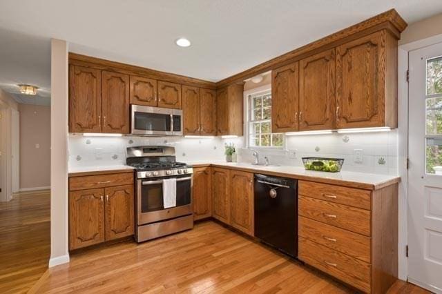 kitchen with light wood finished floors, stainless steel appliances, tasteful backsplash, and brown cabinets