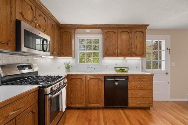 kitchen with brown cabinets, a sink, stainless steel appliances, light wood-type flooring, and tasteful backsplash