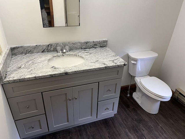 half bath featuring baseboards, vanity, toilet, and wood finished floors