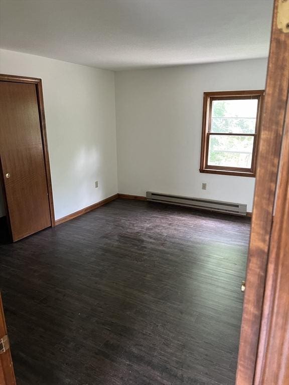 empty room with a baseboard heating unit, dark wood-type flooring, and baseboards