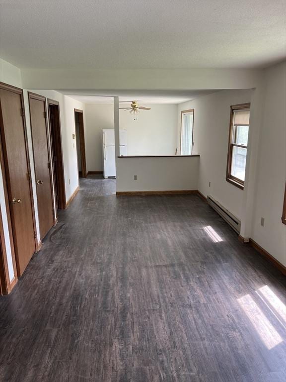 unfurnished living room with a textured ceiling, baseboard heating, dark wood finished floors, and baseboards