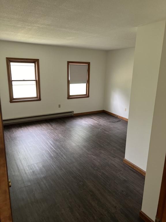 spare room featuring dark wood-style flooring, baseboards, a textured ceiling, and baseboard heating