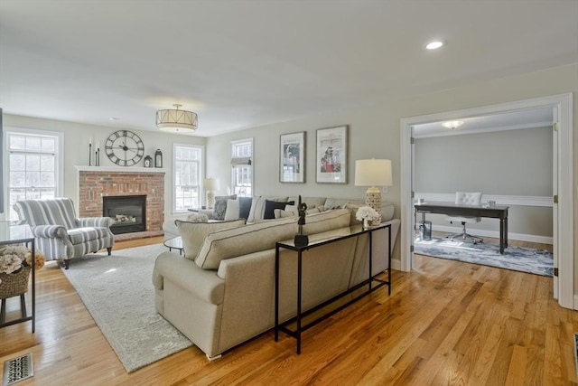 living area featuring light wood-style flooring, a fireplace, visible vents, and a wealth of natural light