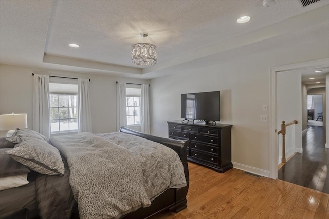 bedroom with a tray ceiling, wood finished floors, and a textured ceiling