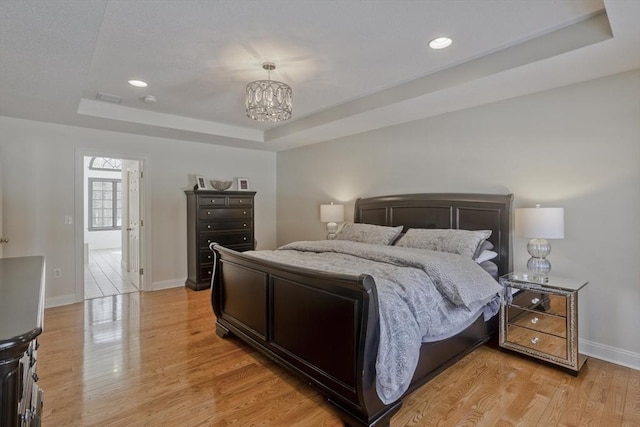 bedroom featuring visible vents, baseboards, a tray ceiling, light wood-style flooring, and an inviting chandelier