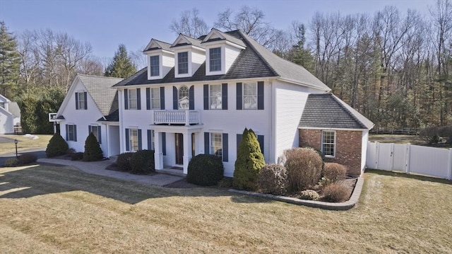 colonial inspired home featuring a front lawn, a gate, a balcony, fence, and brick siding