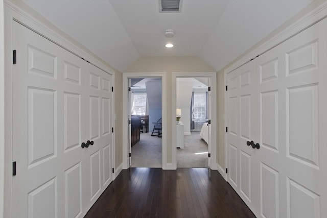 hallway with visible vents, baseboards, dark wood-style flooring, and vaulted ceiling