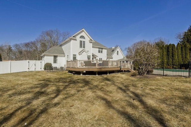 rear view of property featuring a fenced in pool, a wooden deck, a lawn, a fenced backyard, and a gate