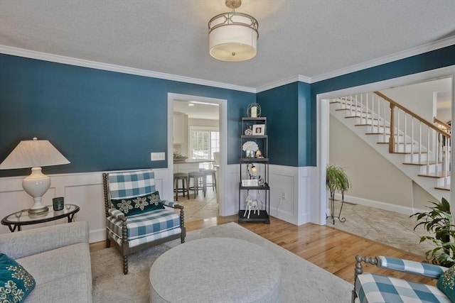 living area featuring crown molding, wood finished floors, a wainscoted wall, and a textured ceiling