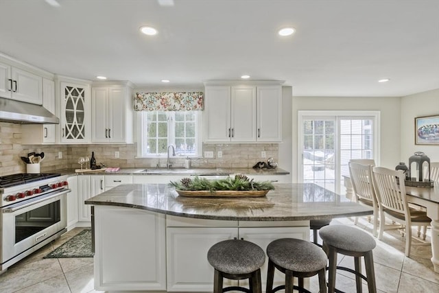 kitchen with a breakfast bar area, light stone countertops, a sink, luxury range, and exhaust hood