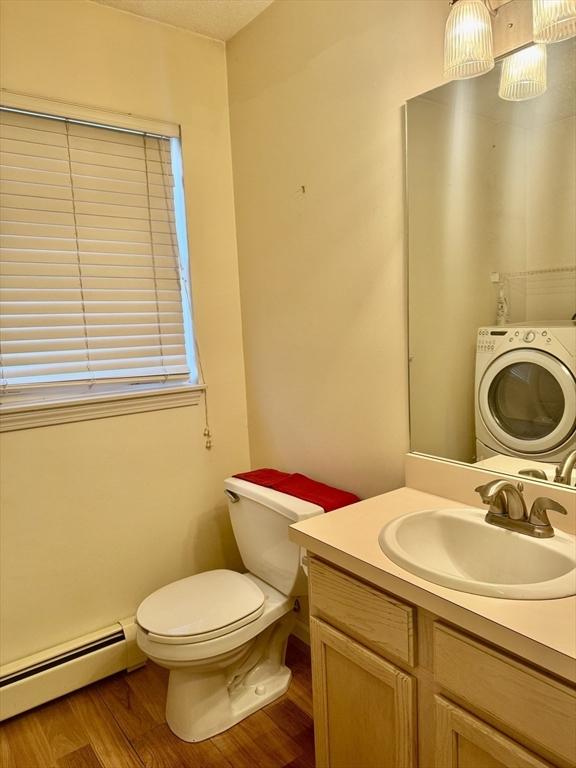 bathroom with baseboard heating, hardwood / wood-style floors, vanity, washer / dryer, and toilet