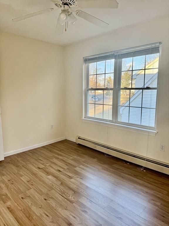 empty room with ceiling fan, a healthy amount of sunlight, baseboard heating, and light hardwood / wood-style flooring