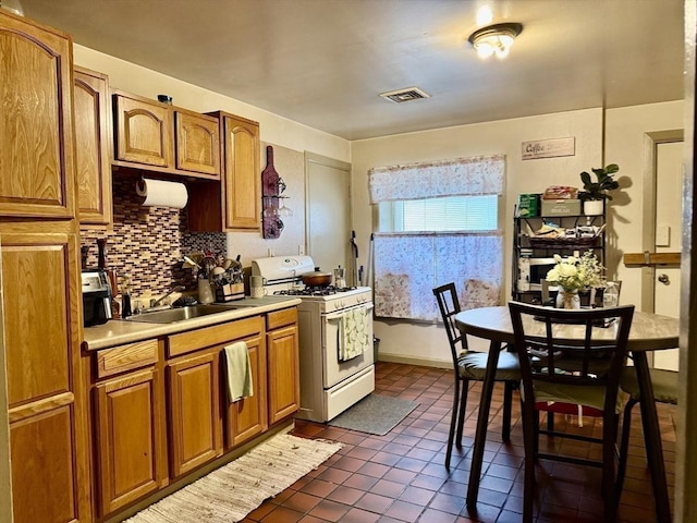 kitchen featuring visible vents, backsplash, dark tile patterned floors, light countertops, and white range with gas stovetop