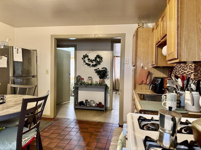 kitchen with tasteful backsplash, white range with gas cooktop, tile patterned flooring, and freestanding refrigerator